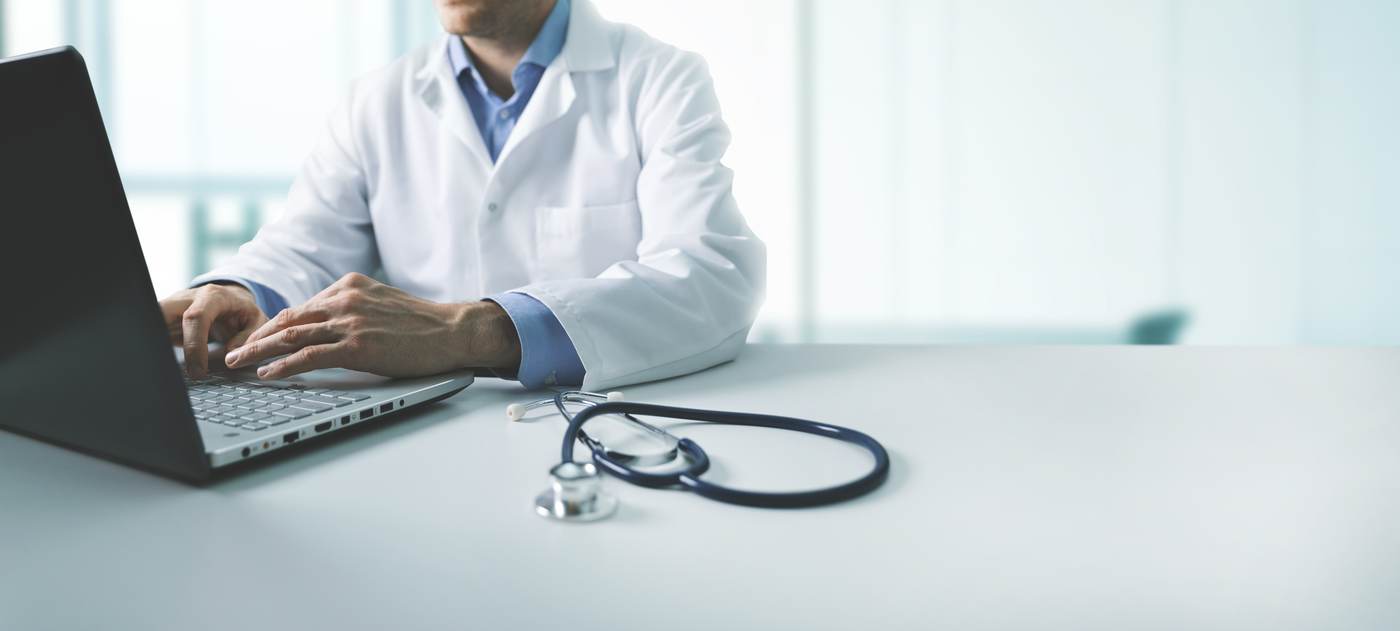 Doctor working on laptop with stethoscope - healthcare IT support for medical practices